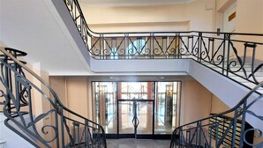 Un escalier en marbre, agrémenté de rampes noires richement décorées, mène à un palier situé au deuxième étage.
