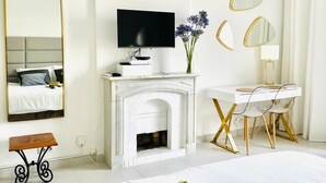 Une chambre à coucher comprenant un lit, une télévision, une cheminée, un bureau avec des chaises et plusieurs miroirs.