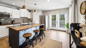 Una cucina moderna con mobili bianchi, un'isola grande con sgabelli e vista su un balcone attraverso porte vetrate.