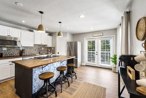 A modern kitchen with white cabinets, a large island with stools, and a view to a balcony through glass doors.