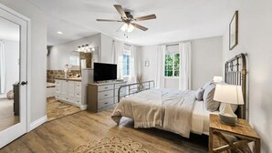 Una camera da letto con un letto, comodino, lampada, ventilatore a soffitto e televisore.