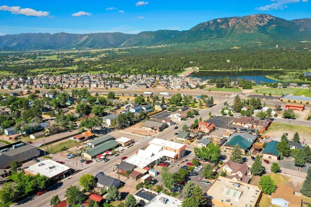An aerial view of a town with a mix of residential and commercial buildings, a bridge, and mountains in the background.