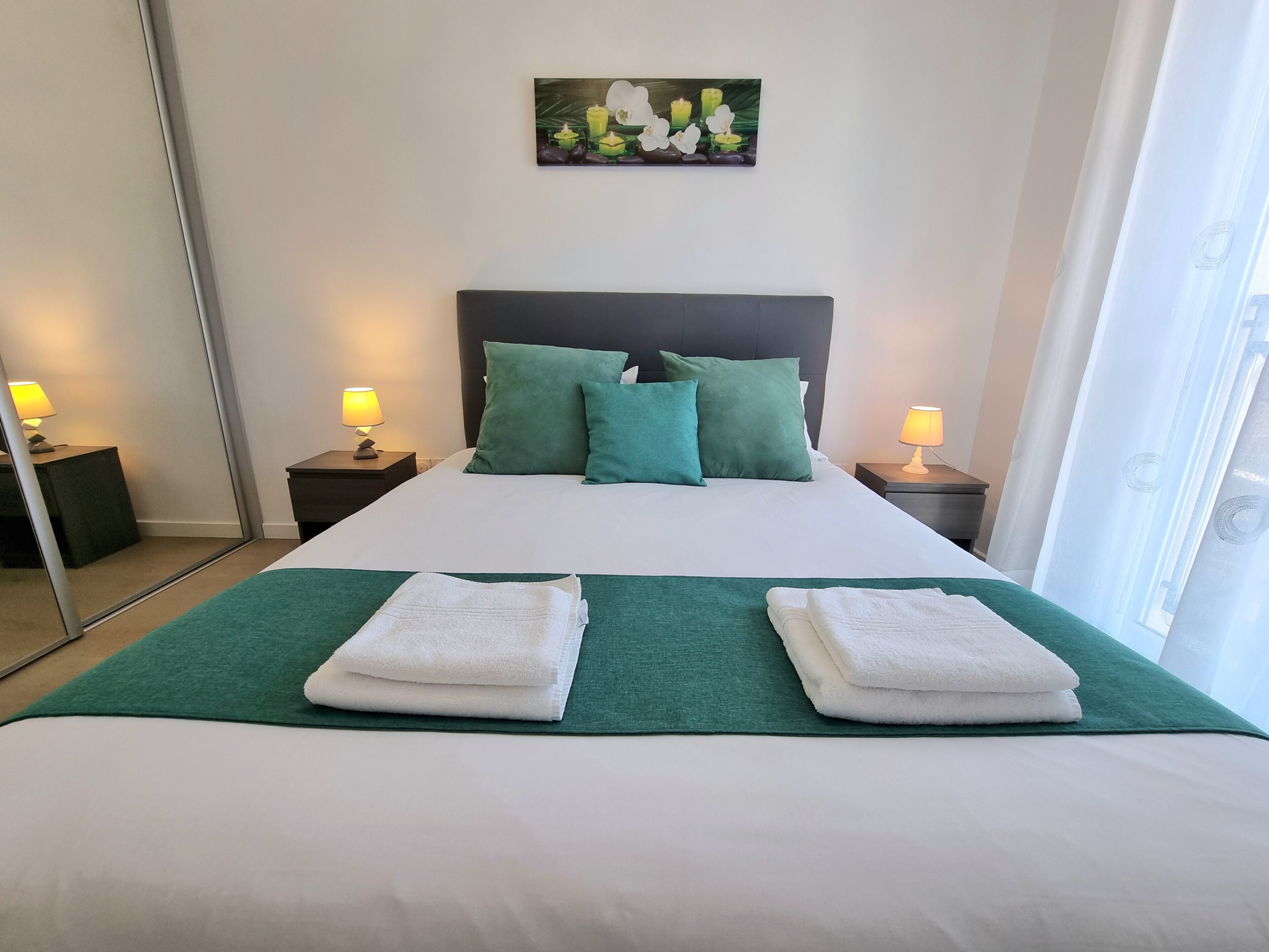 A neatly made bed with green and white bedding, two nightstands with lamps, and a painting on the wall.
