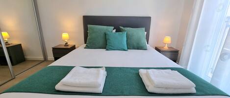 A neatly made bed with green and white bedding, two nightstands with lamps, and a painting on the wall.