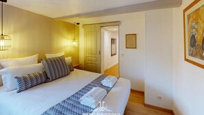 Una camera d'albergo con un letto grande, due lampade ai comodini, un quadro appeso e una porta che dà su un'altra stanza.