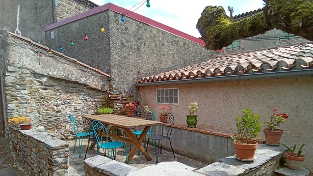 Eine Terrasse mit Steinwänden, einem Holztisch und Stühlen, umgeben von Blumentöpfen.