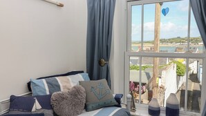 A bedroom with a bed, a window with a view of a coastal town, and a wooden headboard. - Honeymoon Cottage (Bideford)