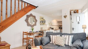 A cozy living room with a grey sofa, wooden coffee table, and a wooden chest of drawers. A wooden staircase leads to an upper level. - Honeymoon Cottage (Bideford)