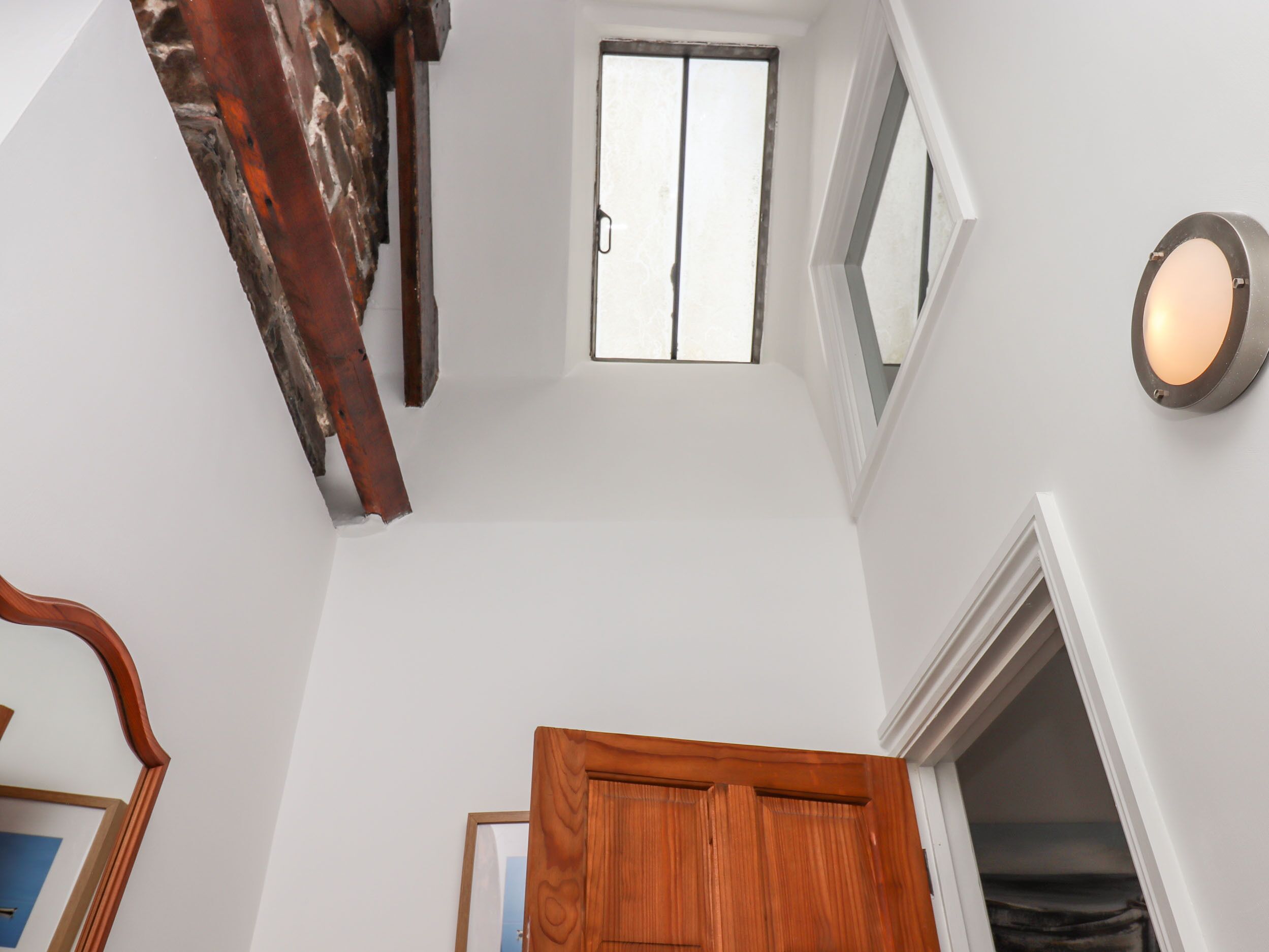 Une pièce avec un plafond haut, une porte en bois, une fenêtre et un luminaire fixé au mur.