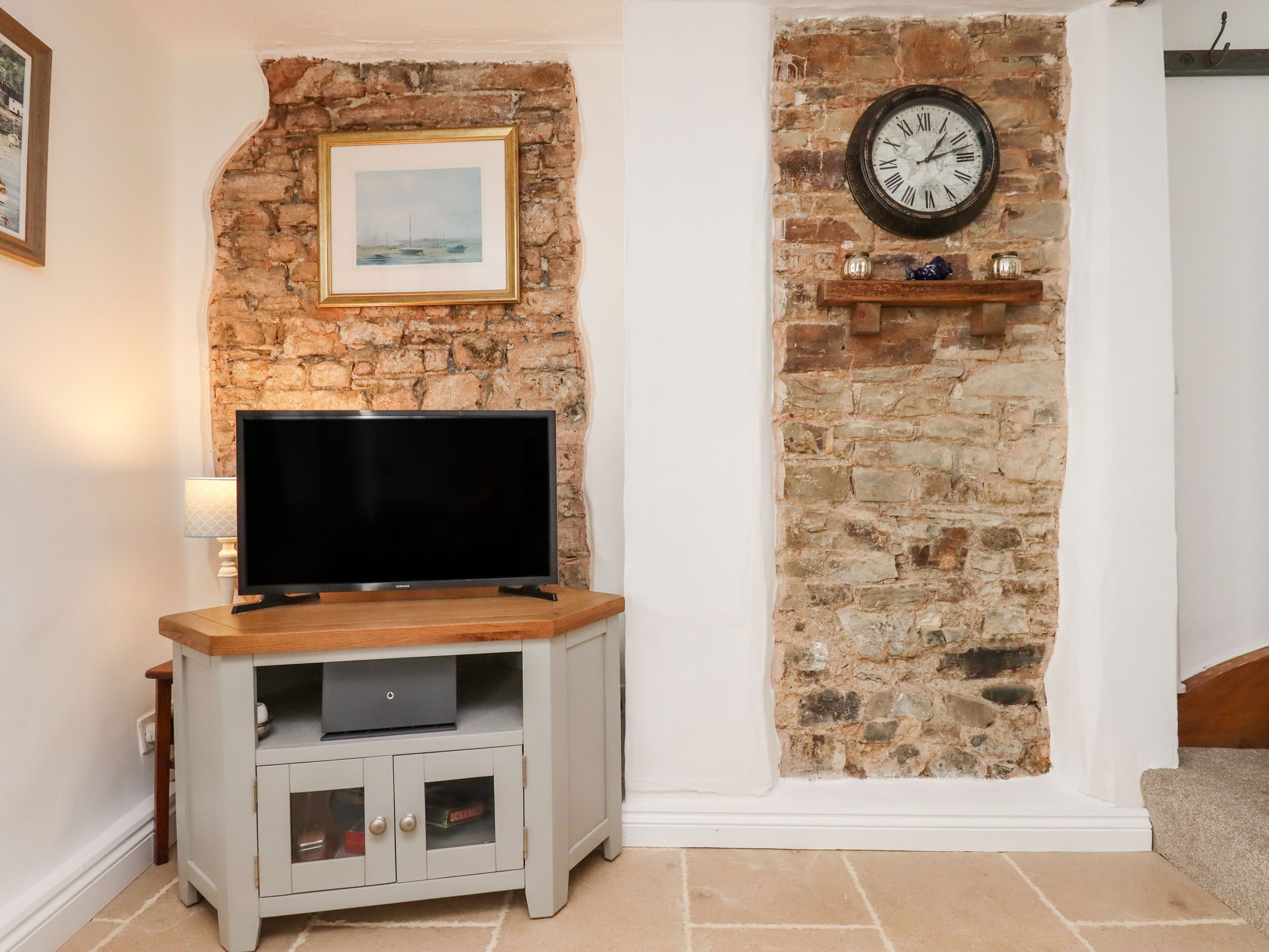 A living room with a stone wall, a mounted clock, a flat-screen TV on a wooden stand, and a small shelf with decorative items.