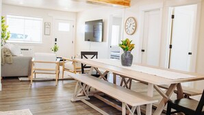 Un vaste espace de vie comprenant une table à manger en bois, des bancs, un canapé et un téléviseur fixé au mur.
