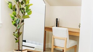 Une chambre à coucher avec un lit, un bureau, une chaise, un miroir et une plante en pot.