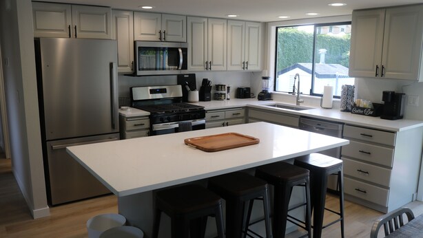 A modern kitchen with white cabinets, stainless steel appliances, and a large island with stools.
