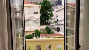Vista desde un balcón con cielo despejado, un árbol y edificios al fondo.