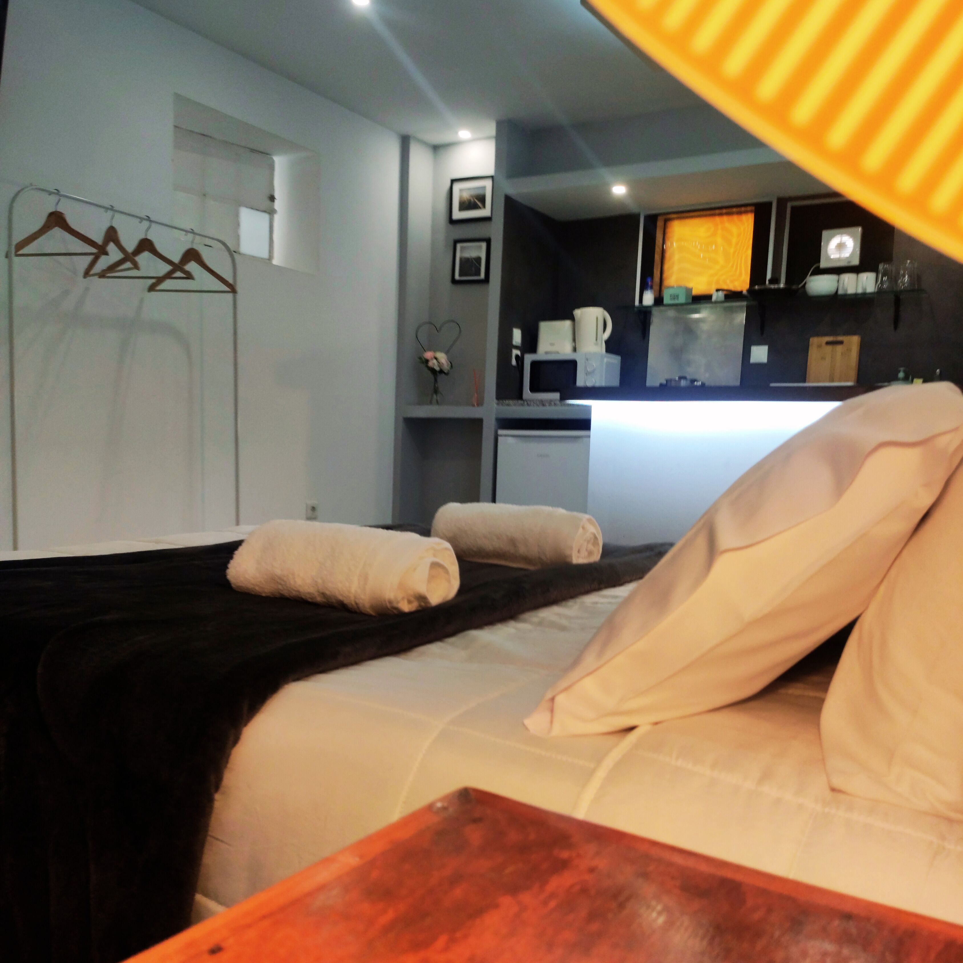 A hotel room with a bed, a wooden table, a kitchen area with a microwave, and a white door.