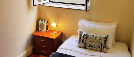 A bedroom with a bed, a bedside table with a lamp, a window, and a radiator.