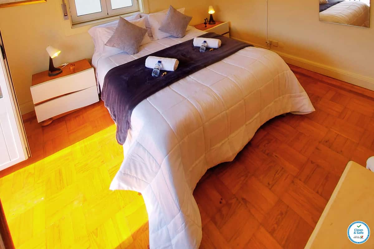 A bedroom with a bed, bedside tables, a TV, and a window with blinds.