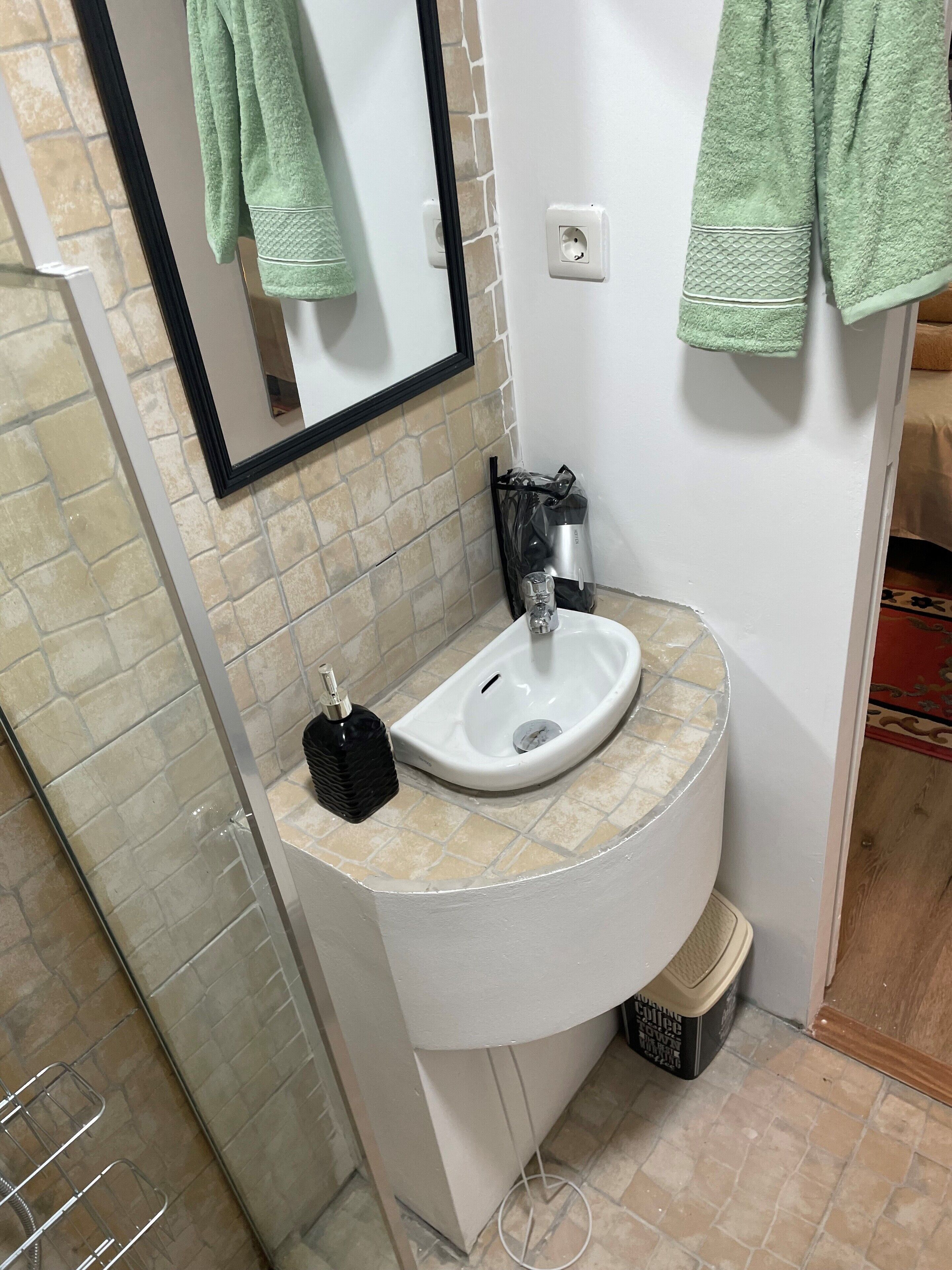 A bathroom with a white sink, a mirror, and a green towel hanging on the wall.