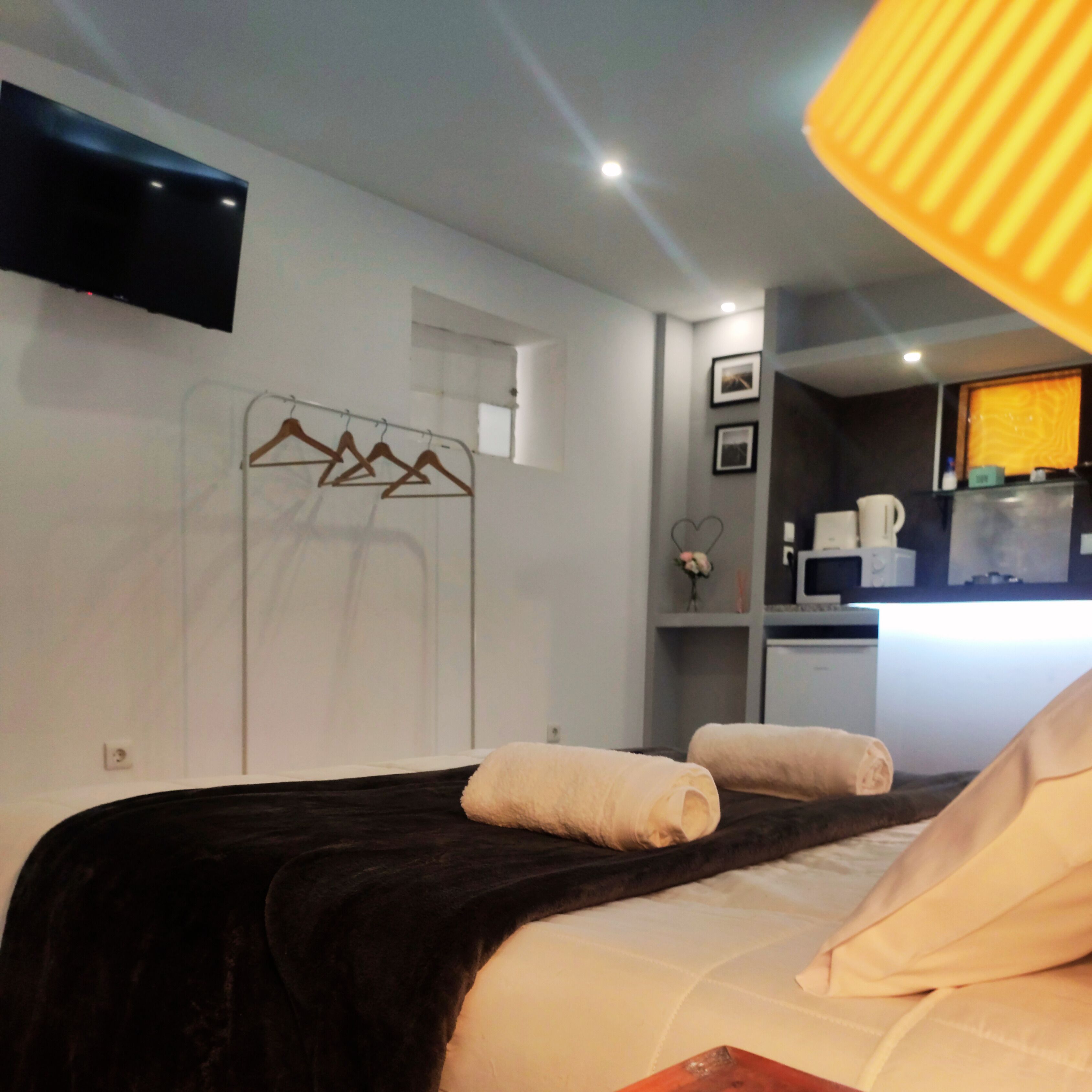 Hotelkamer met een bed, een wandgemonteerde flatscreen-tv, een kitchenette en een badkamer met handdoekhouder.
