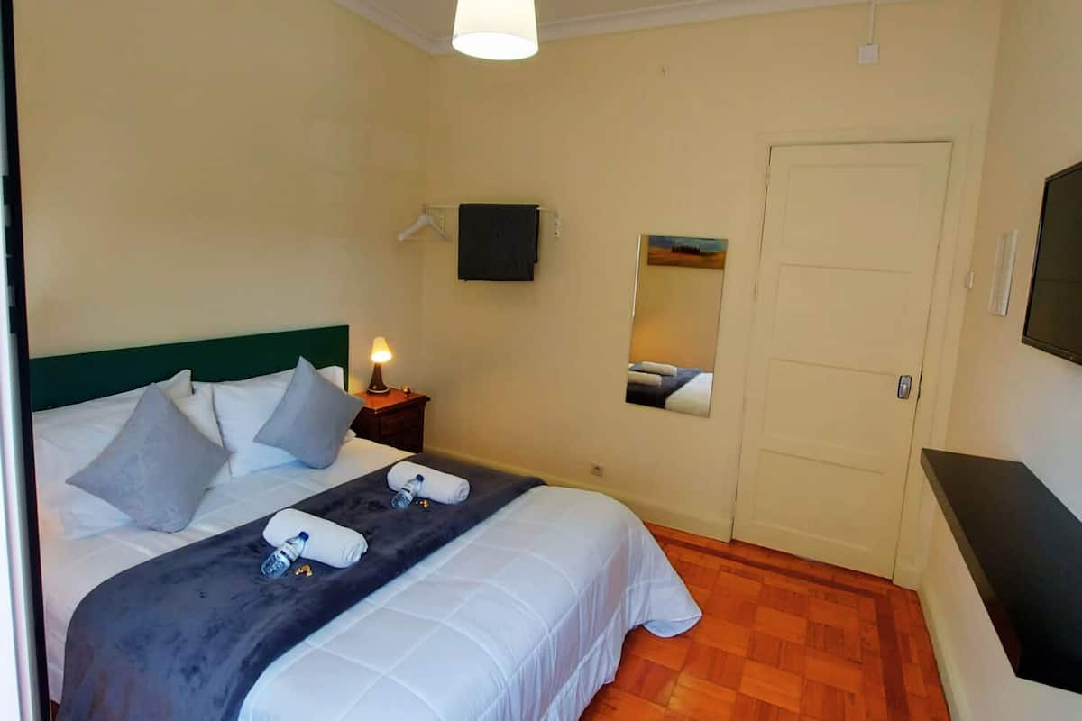 A hotel room with a bed, a nightstand, a TV, a door, and a wooden floor.