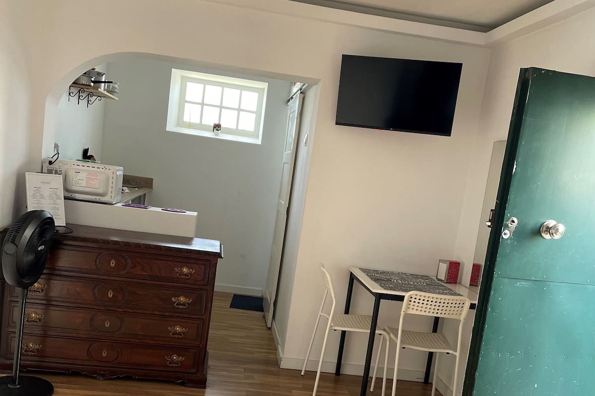 A bedroom with a bed, a dresser, a desk, a chair, a TV, and a window.