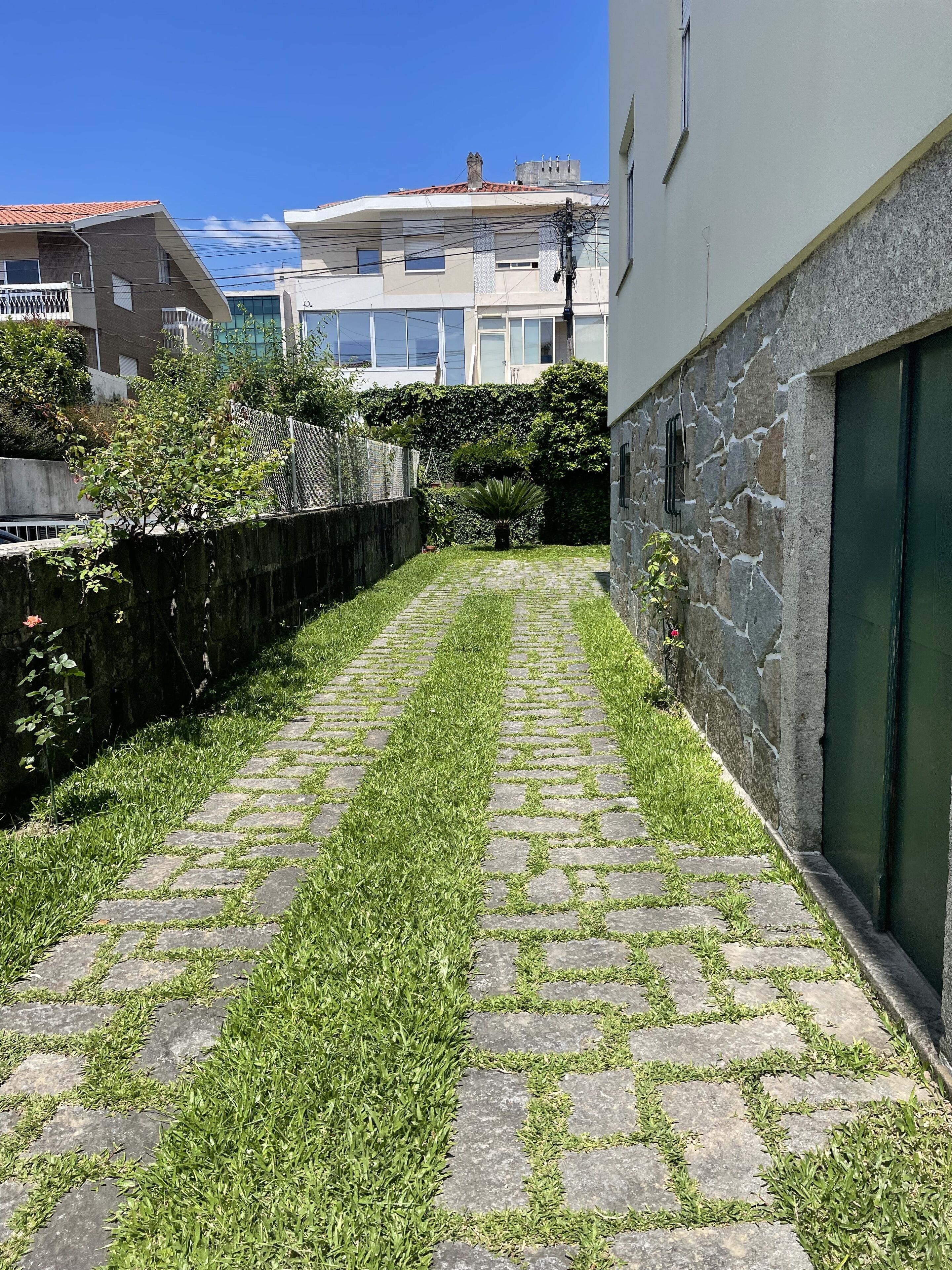 A paved pathway with grass growing in between the stones, bordered by a stone wall and a fence.