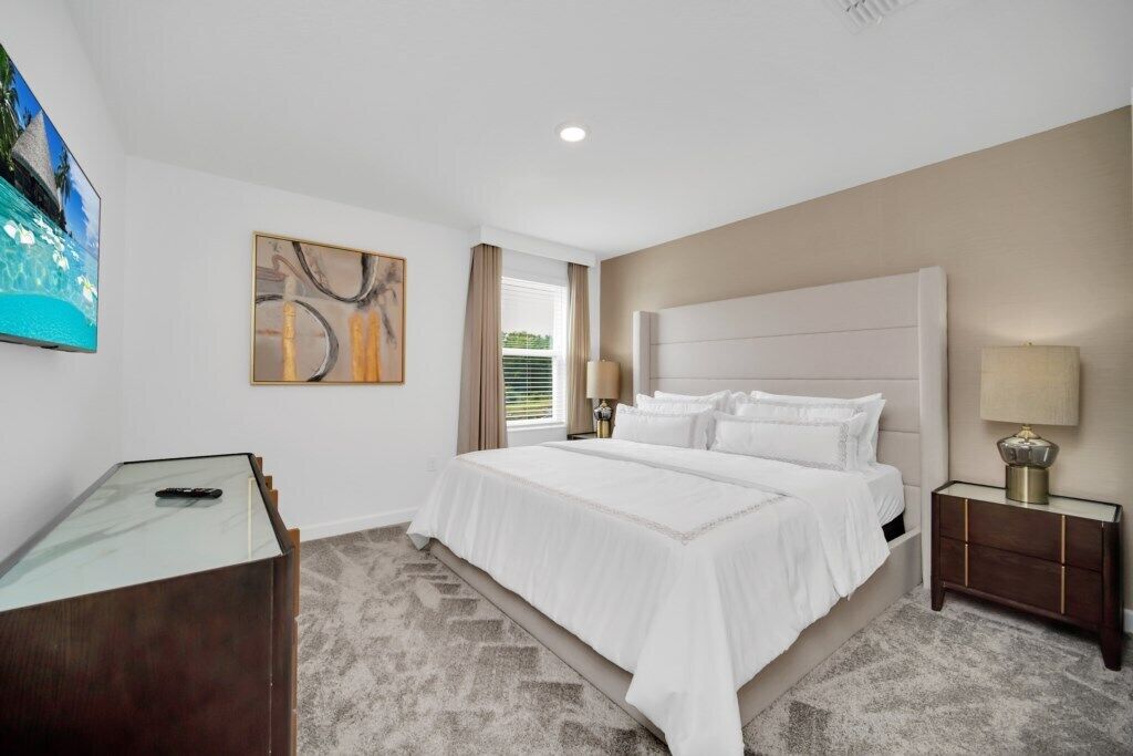 A bedroom with a large bed, a desk, a TV, and artwork on the walls.