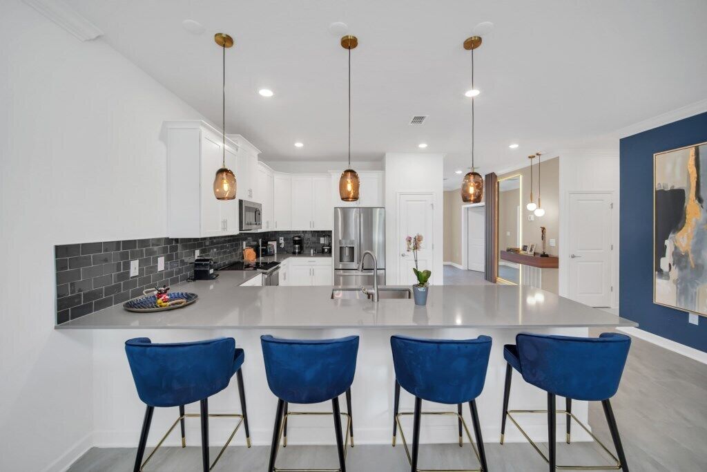 A modern kitchen with a central island, bar stools, pendant lighting, and white cabinetry.