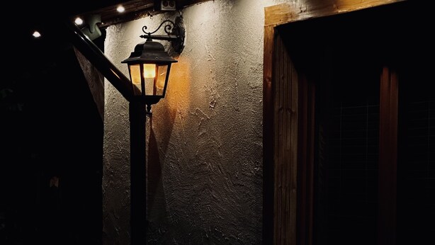En utomhusplats med ett bord och stolar, en väggmonterad lykta och ett fönster med träram.
