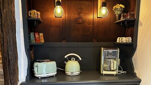 Ett mörkblått kök med en inbyggd hylla ovanför skåpen, där det står en brödrost, en vattenkokare och en kaffebryggare.