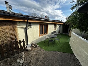 Une maison avec un jardin clôturé, une petite terrasse avec une table et des chaises, et une pelouse verdoyante.
