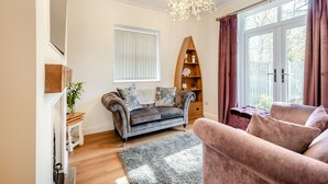A living room with a grey sofa, a pink sofa, a wooden bookshelf, and a chandelier.