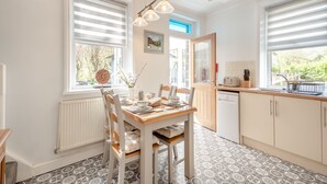 A bright kitchen with a dining table, chairs, and a window with blinds.