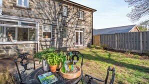 A stone house with a patio table set with plants, a bottle, and glasses.