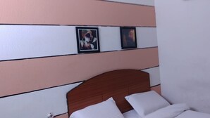 A bedroom with a wooden headboard, white bedding, and two framed pictures on the wall. - Transit Bay  (Rajahmundry)
