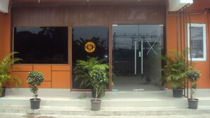 A building entrance with a large glass door, a welcome sign, and potted plants. - Transit Bay  (Rajahmundry)
