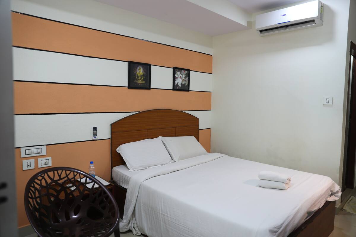 Quarto de hotel com cama, uma cadeira e ar condicionado fixado na parede.