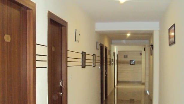 A hallway with wooden doors, a tiled floor, and a light fixture on the ceiling. - Transit Bay  (Rajahmundry)