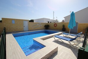 Une piscine aux carreaux bleus, avec des chaises longues et une bouée de sauvetage fixée au mur.