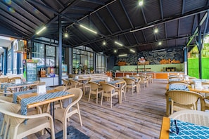Ein Restaurant mit Korbmöbeln, einer Theke mit einer Kreidetafel und Blick auf Grünflächen.