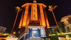 A hotel entrance with a sign reading 'De Mare Family Hotel,' a staircase, and palm trees.