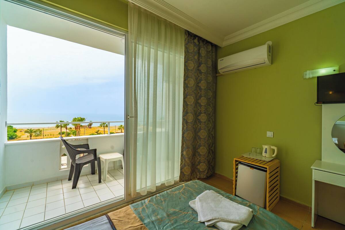 Een hotelkamer met balkon, een bed, een tafeltje, een stoel en een airconditioning.