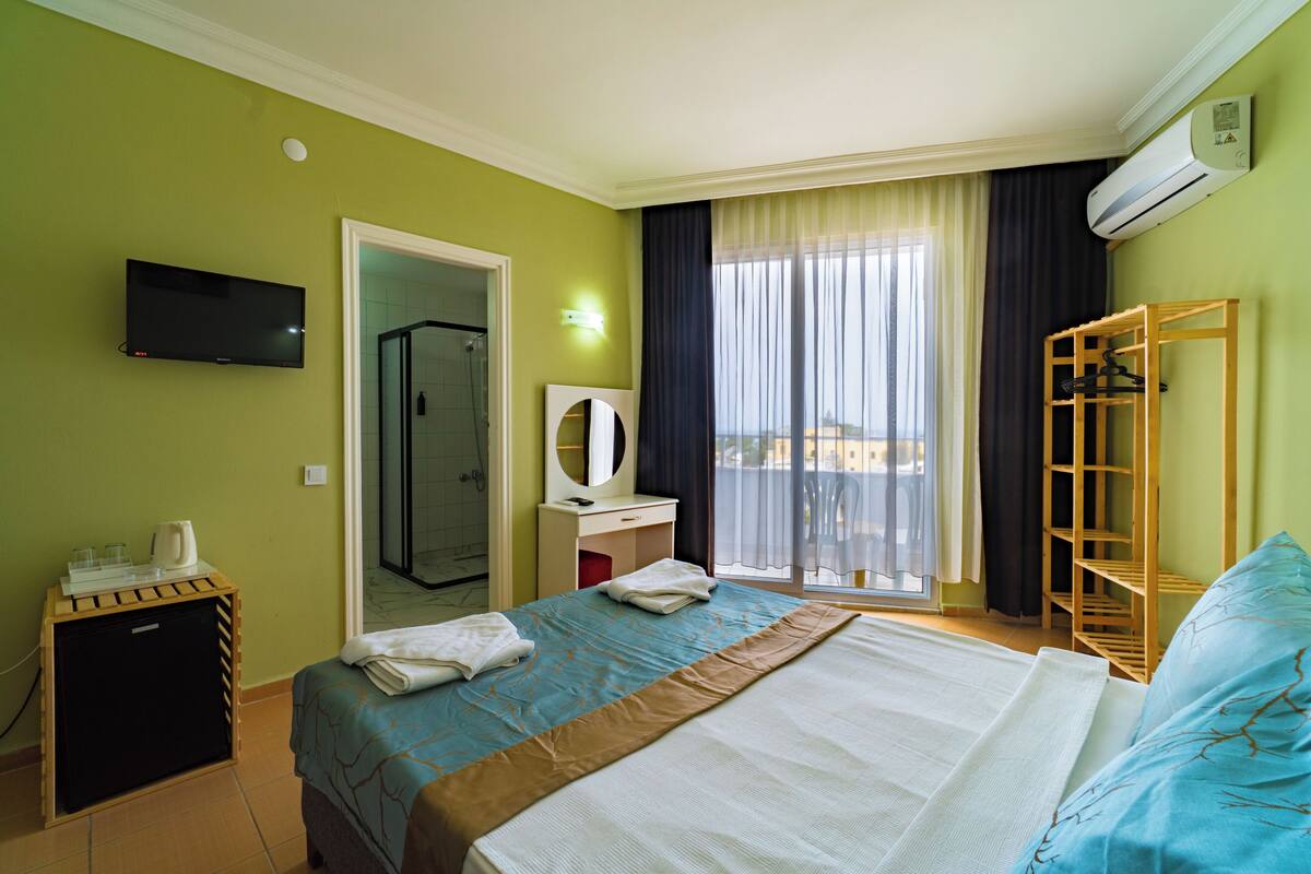 Een hotelkamer met een bed, televisie, bureau, spiegel, kledingkast en een balkon met uitzicht.