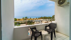 A balcony with two wicker chairs, a small table, and a view of the sea and surrounding landscape.