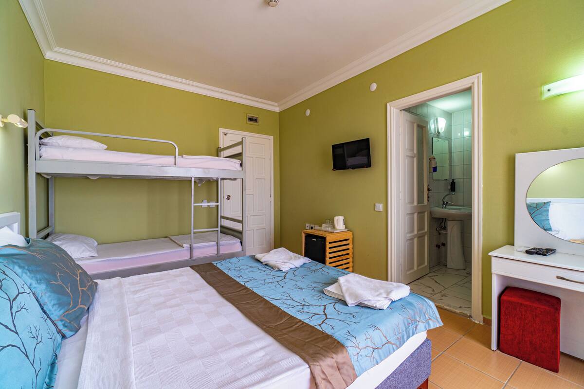 Een kamer met stapelbedden, een bureau met spiegel, een televisie, en een badkamer zichtbaar door een geopende deur.