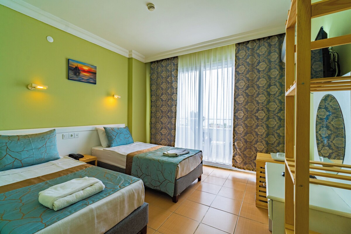 Habitación de hotel con dos camas, un escritorio pequeño, un espejo y una ventana con cortinas estampadas.