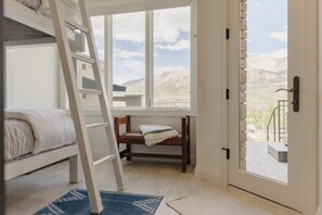 Una habitación con literas, una escalera, una silla pequeña y un ventanal con vistas a las montañas.