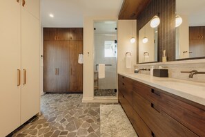 Un baño con piso de piedra, armarios de madera, un espejo grande y una zona de ducha.