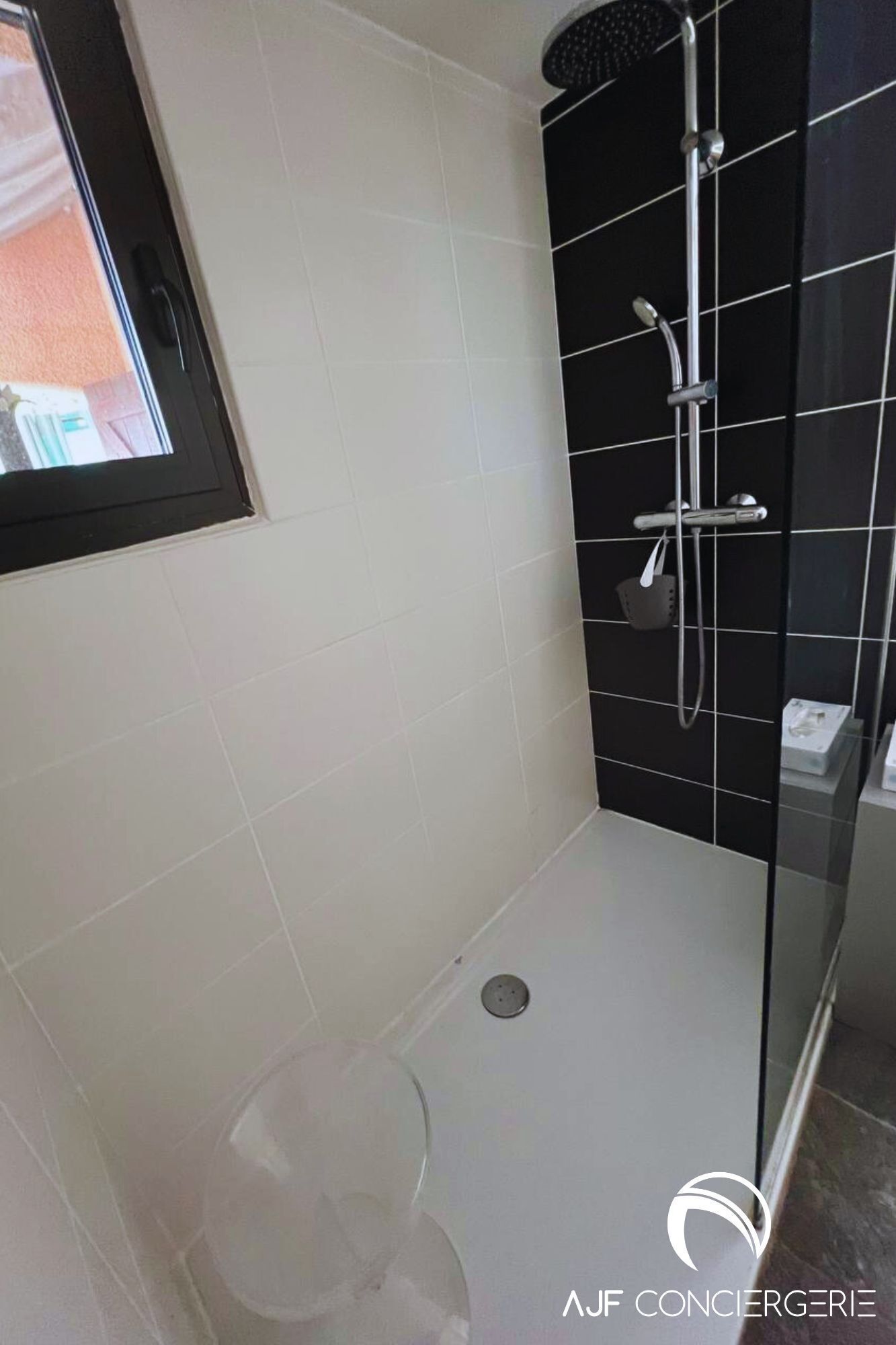 Un baño moderno con cabina de ducha de vidrio, azulejos blancos y una pared de acento con mosaicos negros.