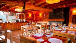 Un comedor de madera acogedor con mesas dispuestas para una comida, una chimenea de piedra y una cocina al fondo.